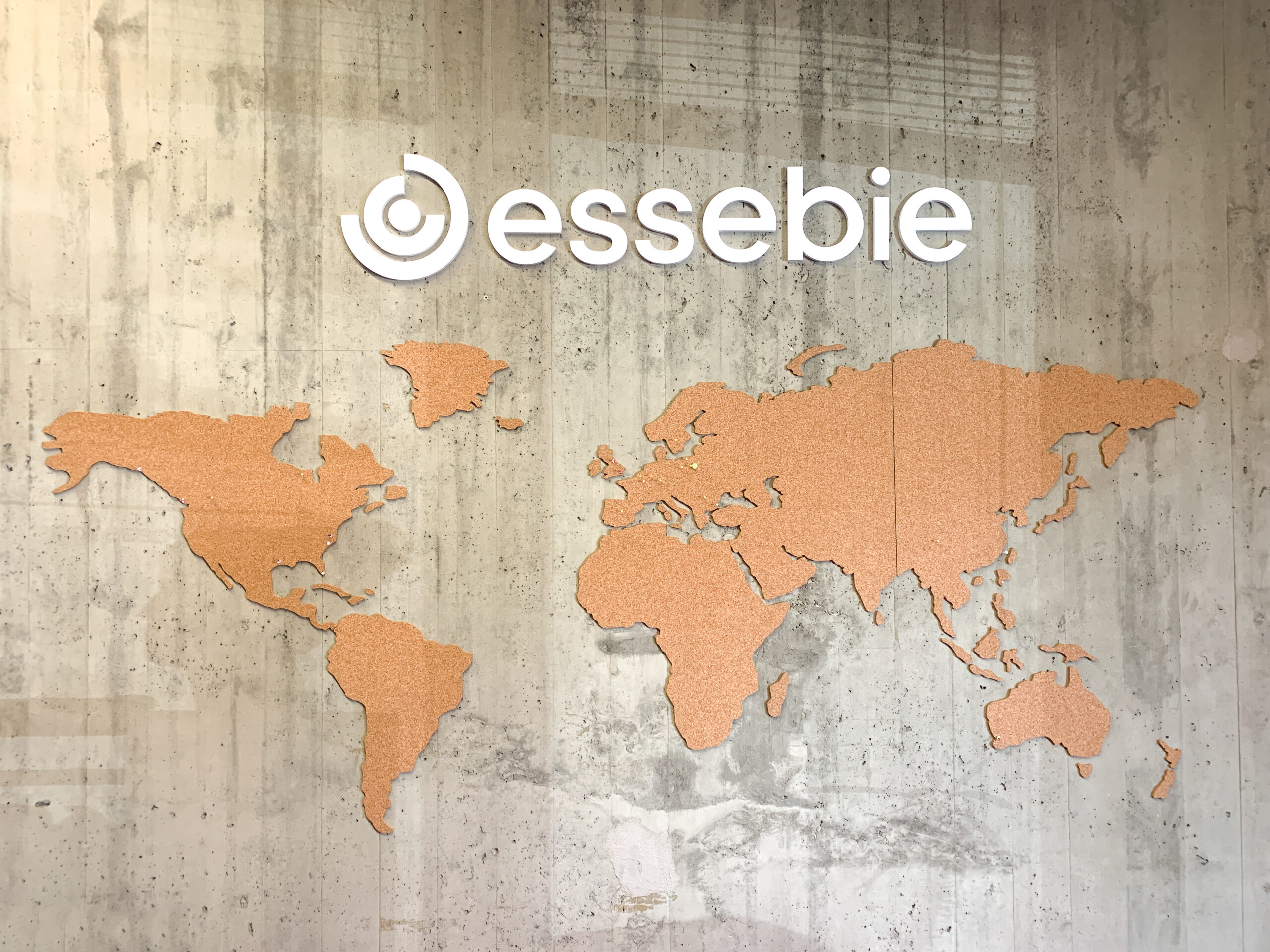 Logo “essebie” su parete in cemento con mappa del mondo in sughero.